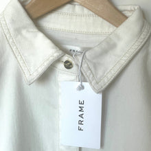 Load image into Gallery viewer, Light-colored shirt with a 'FRAME' tag on a hanger