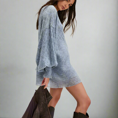 Woman wearing a light blue sweater dress with black boots on a white background