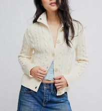 Load image into Gallery viewer, A woman wearing a cream cable-knit button-front cardigan over a light blue denim top and a frayed blue denim mini skirt, photographed against a light gray studio background.