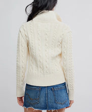 Load image into Gallery viewer, A woman shown from the back wearing a cream cable-knit turtleneck sweater and a blue denim mini skirt against a light gray studio background.