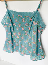 Load image into Gallery viewer, A light blue floral camisole top with thin straps, pink and green floral print, and lace trim at the neckline, hanging against a plain white wall.