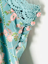 Load image into Gallery viewer, Close-up of a light blue floral dress with a pink and green floral print, featuring a crochet lace yoke and decorative pom-pom buttons.