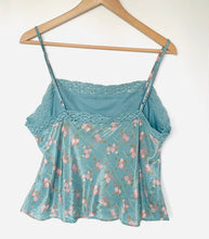 Load image into Gallery viewer, A light blue floral camisole top with lace trim and thin straps, hanging on a wooden hanger against a plain white wall.