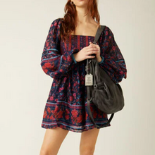 Load image into Gallery viewer, Woman wearing a patterned dress holding a black bag against a plain background