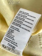 Load image into Gallery viewer, A close-up of a white fabric care label sewn onto a pale yellow or cream-colored garment, showing text including '100% POLYESTER' and 'MADE IN INDIA'.