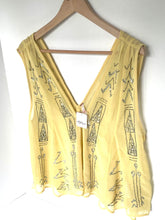 Load image into Gallery viewer, A pale yellow sleeveless V-neck top with black rhinestone geometric patterns, hanging on a wooden hanger against a white wall.