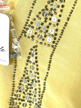 Load image into Gallery viewer, A close-up of a yellow garment or fabric decorated with metallic silver sequins and bead strands, with a small clear plastic bag of embellishments partially visible on the left.