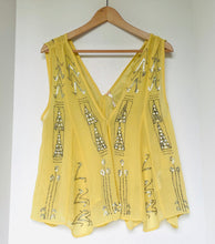Load image into Gallery viewer, A yellow sleeveless V-neck top with silver sequin and bead geometric patterns, hanging on a wooden hanger against a plain white wall.