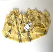 Load image into Gallery viewer, A light yellow scarf with a black Eiffel Tower pattern, featuring a white product tag attached, laid out on a white surface.