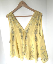 Load image into Gallery viewer, A pale yellow sleeveless blouse with silver rhinestone embellishments, hanging on a wooden hanger against a white wall.