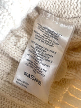 Load image into Gallery viewer, A close-up of a white cotton laundry care label with black printed instructions and symbols, resting on a cream-colored textured knit fabric.