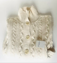Load image into Gallery viewer, A folded cream-colored cable-knit sweater vest with three buttons, shown on a plain white background with a paper tag attached.