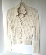 Load image into Gallery viewer, An off-white cable-knit cardigan sweater with a mock neck and button closure, hanging on a wooden hanger against a white background.