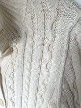 Load image into Gallery viewer, Close-up of a cream-colored cable-knit cardigan sweater showing the detailed knit texture and buttons.