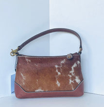 Load image into Gallery viewer, A brown and white cowhide shoulder bag with solid brown leather trim and a gold-tone clasp, set against a white background.