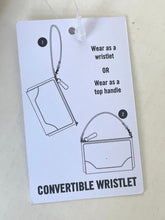 Load image into Gallery viewer, A white product tag with black line drawings and text showing a convertible wristlet, including instructions to wear as a wristlet or top handle and the words 'CONVERTIBLE WRISTLET' at the bottom.