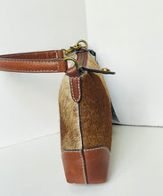 Load image into Gallery viewer, A close-up side view of a handbag featuring a brown and beige cowhide body with smooth brown leather trim, a brown shoulder strap, and brass-tone hardware, set against a plain white background.