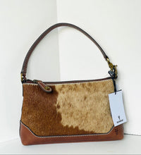 Load image into Gallery viewer, A shoulder handbag with a brown and beige cowhide patterned body, brown leather trim, and a single top handle, shown with a white product tag hanging from the side against a white background.