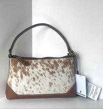 Load image into Gallery viewer, A small handbag with a brown and white cowhide patterned body, brown leather trim, and a dark brown top handle, shown with two white tags against a plain light gray background.