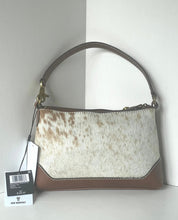 Load image into Gallery viewer, A handbag with a brown and white cowhide patterned body, brown leather trim and handle, and gold-tone hardware, shown with a retail tag against a white background.
