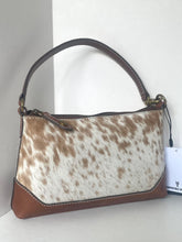 Load image into Gallery viewer, A shoulder handbag with a brown and white cowhide patterned body, dark brown leather trim, and a dark brown top handle, shown against a plain light background with a hangtag visible on the right.