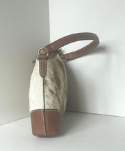 Load image into Gallery viewer, A small shoulder bag with a brown and white cowhide body, brown leather trim, and a brown shoulder strap, shown standing in a white corner.