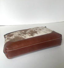 Load image into Gallery viewer, A small zippered pouch featuring a brown leather base and a cowhide-patterned top panel in brown and white, with visible contrast stitching.