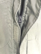 Load image into Gallery viewer, Close-up of a light olive green utility jacket showing the front zipper, hook-and-loop closure, and fabric texture.