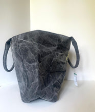 Load image into Gallery viewer, A dark gray waxed canvas tote bag with a textured, distressed finish, featuring two loop handles and a small hanging tag, set against a plain off-white background.