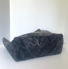 Load image into Gallery viewer, A black velvet cosmetic pouch with a gold-tone logo plaque on the front, photographed on a white surface against a white background.