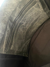 Load image into Gallery viewer, A close-up of a dark gray distressed leather jacket with a diagonal zipper, showing the textured leather grain and stitching.