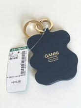 Load image into Gallery viewer, A black leather keychain bag with gold-tone hardware, featuring the brand name 'GANNI' printed in gold on the back. It is shown with its original white Simons retail tag on a plain white background.