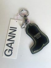 Load image into Gallery viewer, A GANNI keychain with a black leather boot-shaped charm featuring yellow contrast stitching, a silver split keyring, and a white paper tag with the GANNI logo.