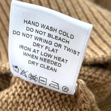 Load image into Gallery viewer, Clothing label with care instructions on a knitted fabric background