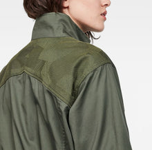 Load image into Gallery viewer, Close-up side profile of a person wearing an olive green jacket with a textured, patterned shoulder yoke and a high collar, set against a plain white background.