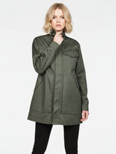 Load image into Gallery viewer, A woman wearing an olive green utility jacket with a high collar and front pockets, paired with black pants, against a plain light gray background.