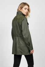 Load image into Gallery viewer, A woman wearing an olive green utility-style jacket with contrasting darker green shoulder panels, shown from a side-back angle against a plain light gray studio background.