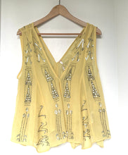 Load image into Gallery viewer, A pale yellow sleeveless V-neck top with silver rhinestone embroidery, hanging on a wooden hanger against a plain white wall.