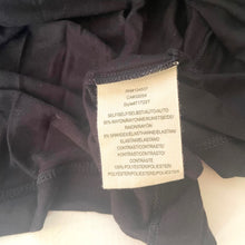 Load image into Gallery viewer, Clothing label on a dark fabric background