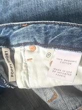 Load image into Gallery viewer, Close-up of denim fabric with a label indicating organic cotton and made in the USA.