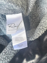 Load image into Gallery viewer, Close-up of a label on a textured fabric with 'Rai' branding.