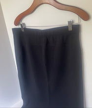 Load image into Gallery viewer, A close-up of a black skirt or dress section hanging from a wooden hanger against a plain light background.