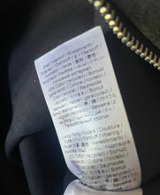 Load image into Gallery viewer, Close-up of a sewn-in care label inside a black garment, showing printed care instructions and symbols on a white tag next to a gold zipper.