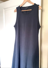 Load image into Gallery viewer, A sleeveless dark navy blue dress hanging on a wooden hanger against a white door and beige wall.