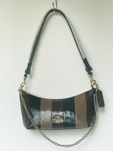 Load image into Gallery viewer, A Coach crescent-shaped shoulder bag in black and brown patent leather with a gold-tone chain strap and a black leather hangtag, hanging against a plain white wall.