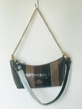 Load image into Gallery viewer, A Coach shoulder bag with brown and black vertical stripes, featuring a gold-tone chain strap and a silver-tone shoulder strap, hanging against a plain white wall.