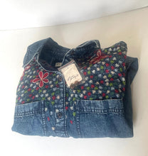 Load image into Gallery viewer, A folded denim shirt jacket featuring a floral printed front panel with red, white, and green flowers, and a solid blue denim lower section and sleeves, with a paper tag attached.