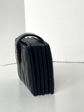 Load image into Gallery viewer, A black quilted leather clutch handbag with a top handle and gold-tone hardware, photographed on a light gray floor against a white wall.