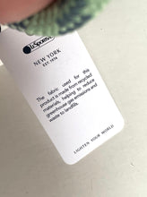 Load image into Gallery viewer, A close-up of a white product tag attached to a garment, showing the brand name 'Lisports' and text about recycled fabric, on a light neutral background.