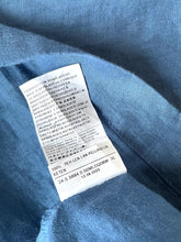 Load image into Gallery viewer, Close-up of a blue fabric garment showing an interior sewn-in care label with printed text details.
